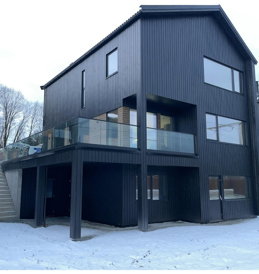 Nybygd enebolig i tre etasjer med sort trekledning og glassrekkverk, oppført av Danielsen Bygg AS i Sandnes